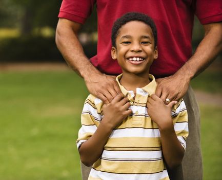 Father standing behind son with hands on his shoulders as boy smiles.