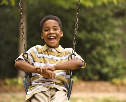 Happy smiling boy on swing in park playground.