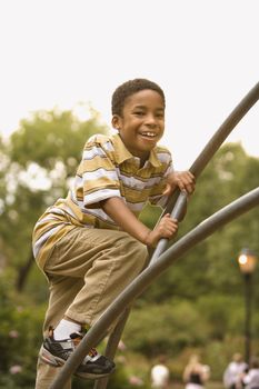 Boy climbing metal bars on playground in park smiling.