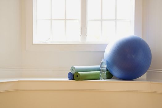 Balance ball, exercise mats and bottled water at gym by window.