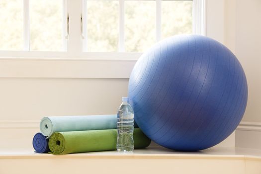 Balance ball, exercise mats and bottled water at gym by window.