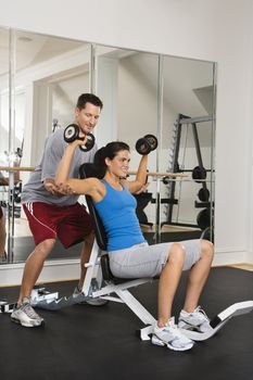 Man assisting woman at gym with hand weights smiling.