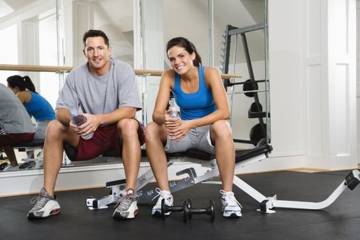 Man and woman sitting on exercise machine talking holding water bottles.