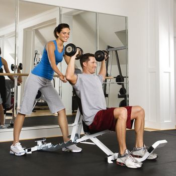 Woman spotting man lifting weights at gym.