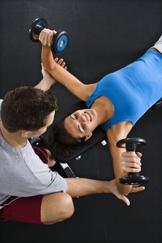 Man assisting woman lifting weights at gym.