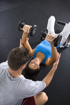 Man assisting woman lifting weights at gym.