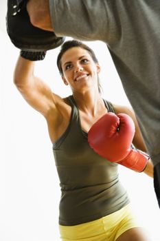 Woman wearing boxing gloves hitting training mits man is holding.