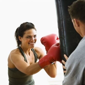 Woman wearing boxing gloves hitting training mits man is holding.