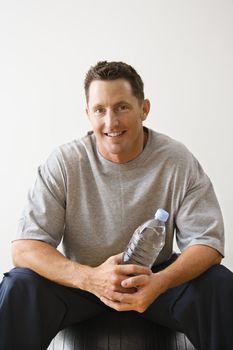 Man holding water bottle sitting on balance ball at gym smiling.