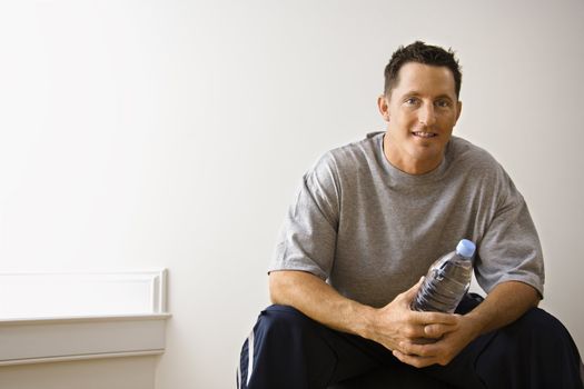 Man holding water bottle sitting on balance ball at gym smiling.