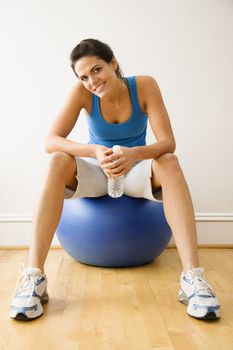 Woman holding water bottle sitting on balance ball at gym smiling.