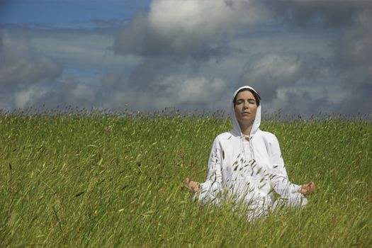 Beautiful athletic woman making yoga on a green meadow