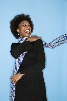 Half length studio portrait of smiling happy woman flinging scarf over shoulder on blue background.
