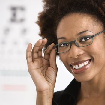 Portrait of woman with afro wearing eyeglasses with medical eyechart in background.