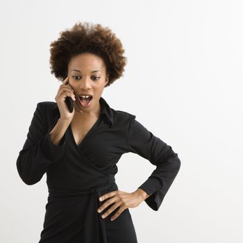 Woman talking on cellphone looking shocked against white background.
