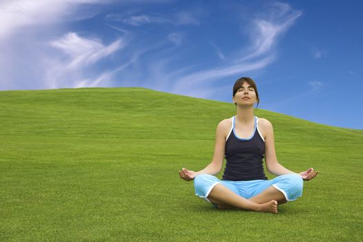 Beautiful athletic woman making yoga on a beautiful green meadow