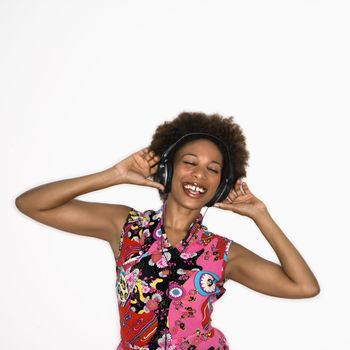 Woman with afro wearing vintage print fabric and listening to headphones smiling and dancing.