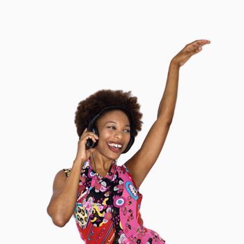 Woman with afro wearing vintage print fabric and listening to headphones smiling and dancing.