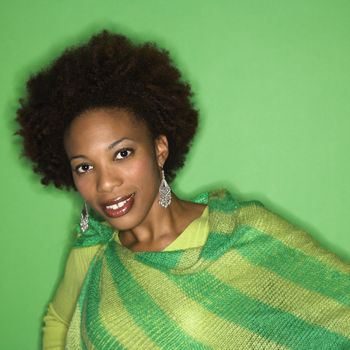 Portrait of woman with afro wearing green striped shawl on green background smiling.