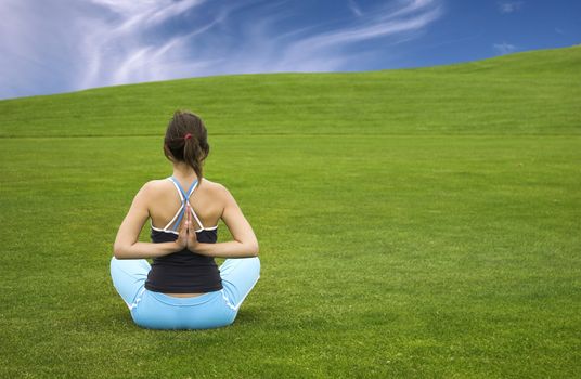 Beautiful athletic woman making yoga on a beautiful green meadow