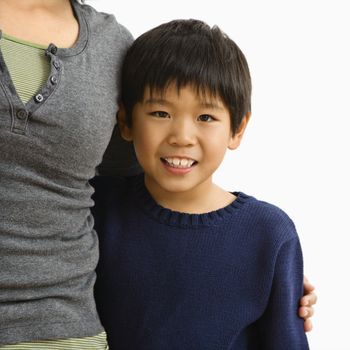 Boy standing smiling with mother standing next to him with arm around him.