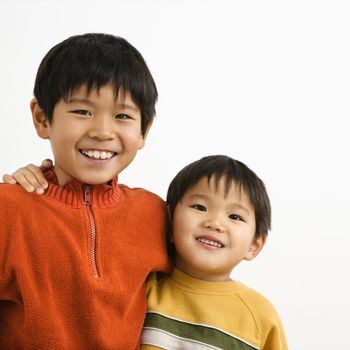 Portrait of young Asian brothers with arms around eachother smiling.