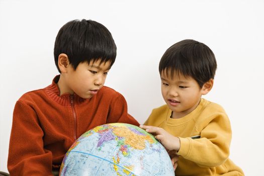 Two Asian boys looking and pointing at world globe