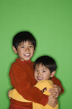 Young Asian brothers hugging eachother smiling.