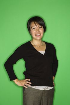 Portrait of smiling Asian woman standing with hands on hips against green background.