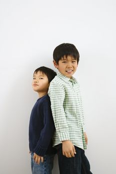 Two young Asian brothers standing back to back.