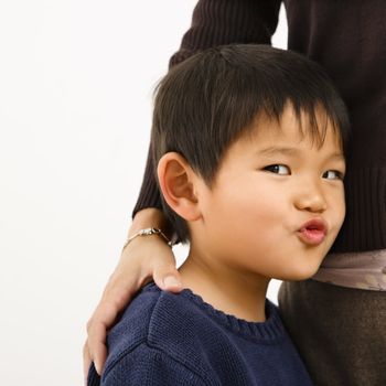 Young Asian boy making funny face standing next to mother.