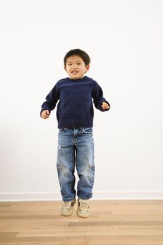 Young Asian boy jumping up into air smiling.