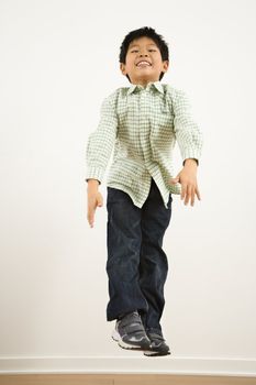 Young Asian boy jumping up into air smiling.