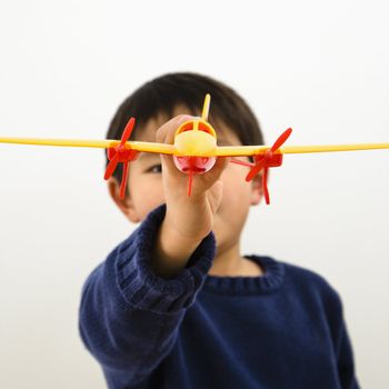 Young Asian boy playing with plastic toy airplane.