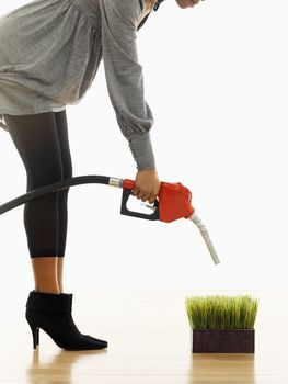 Woman holding gasoline pump nozzle over green grass.