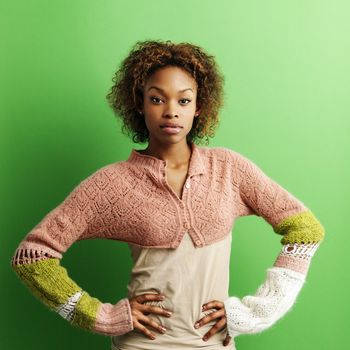 Portrait of pretty young woman standing against green background with hands on hips.