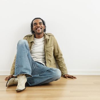 Man sitting on wood floor of home smiling.