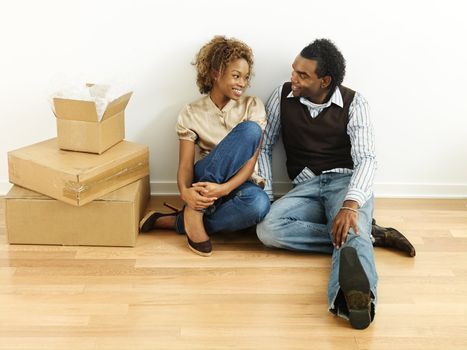 Portrait of smiling happy young couple sitting on floor of home with moving boxes.