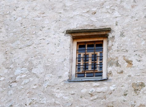 Old closed window with bars on a stone wall.