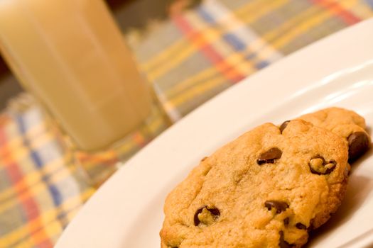 chocolate chip cookies on a white plate in front of a glass of milk