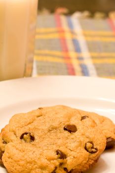 chocolate chip cookies on a white plate in front of a glass of milk