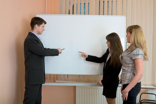 Office workers discuss work standing at a board