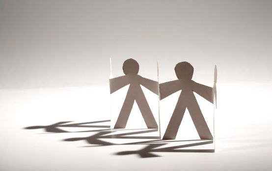 Line of cutout paper dolls throwing a shadow