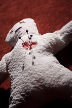 White Voodoo Doll with Pins in its Heart on Red Background