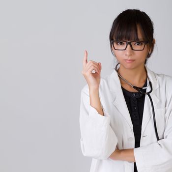 Confident Chinese medical doctor holding finger with serious expression, closeup portrait with copyspace on gray.
