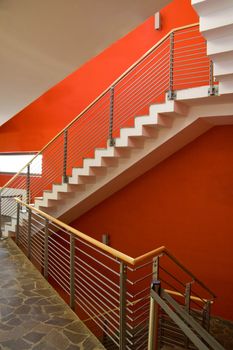 Staircase with red wall and fence going upstairs.