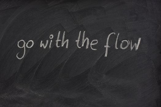 go with the flow phrase handwritten with white chalk on blackboard with erase smudge patterns