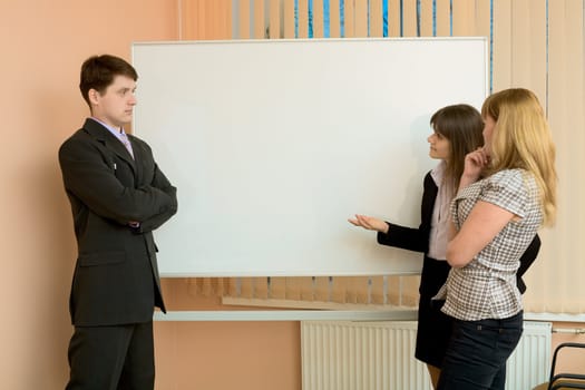 Office workers discuss work standing at a board