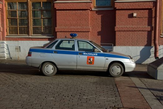 Police car on a cobblestone road near a building from a red brick