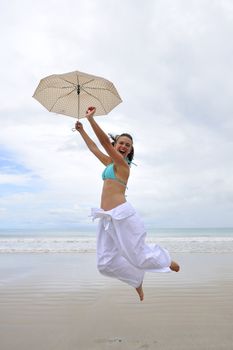 woman jumping on a tropical beach holding an umbrella 
